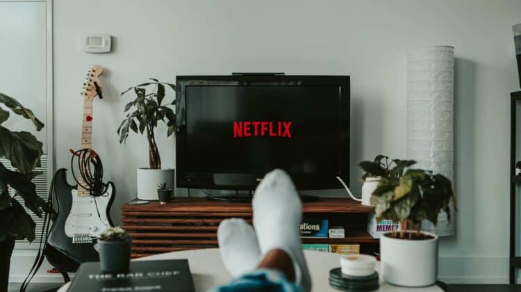 Person relaxing on a couch with a laptop, enjoying Netflix streaming on the screen.